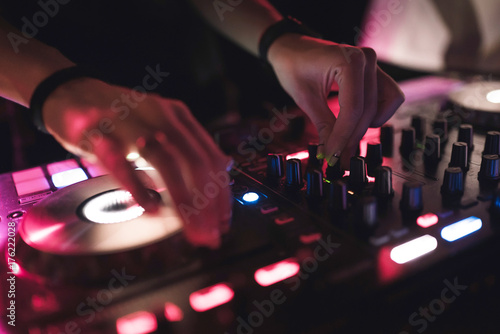 Hands of woman DJ tweak various track controls on dj's deck at night club 