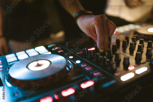Hands of woman DJ tweak various track controls on dj's deck at night club 