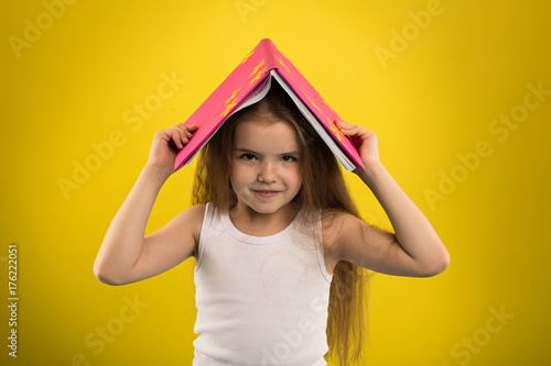 Concept - education. Girl reading a book in a pink cover, shooting in the studio on an isolated yellow background