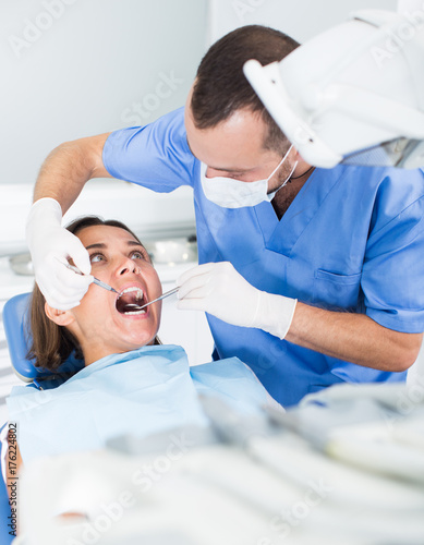 Dentist is treating female patient which is sitting in dental chair