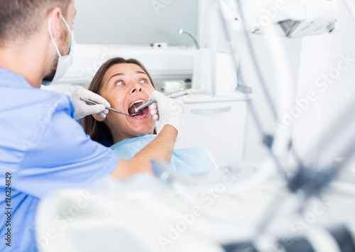 Dentist is treating woman patient which is sitting chair in clinic