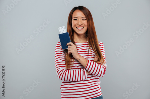 Happy asian woman in sweater holding passport with tickets