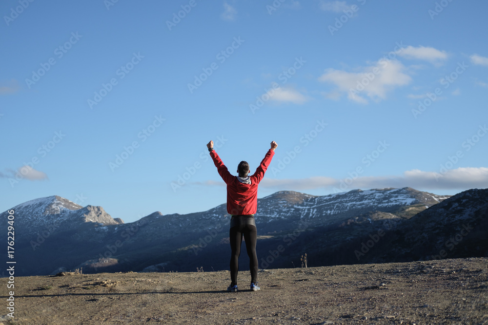 Back view of successful sporty man celebrating training goals towards and freedom on the mountain and sky in late winter.