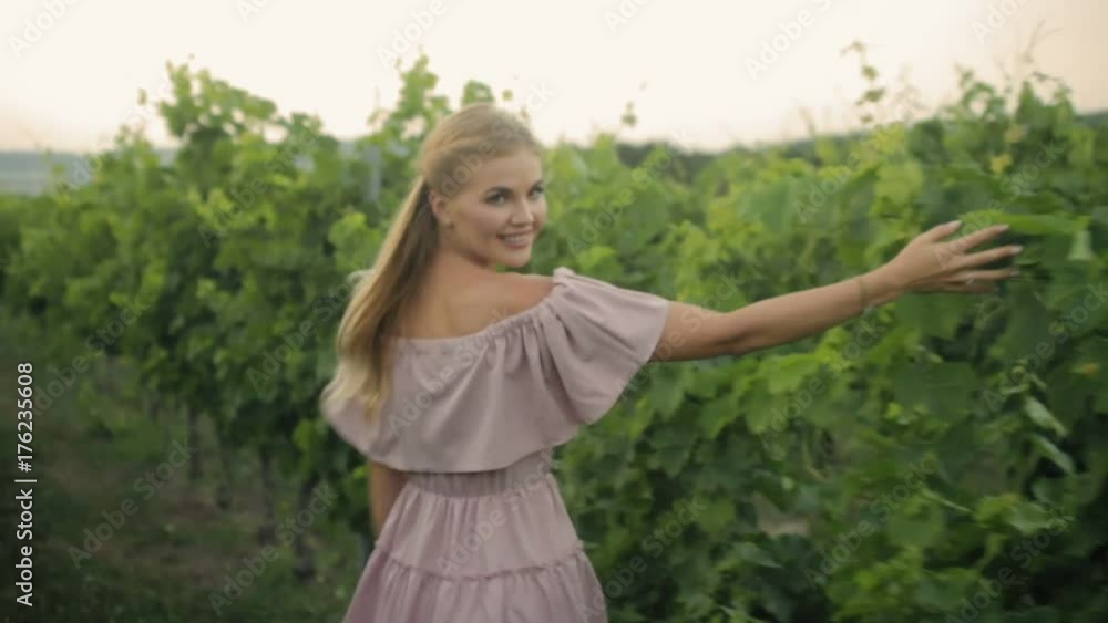 Tender blonde in the pink dress walking along the green vineyard Tender blonde in the pink dress walking along the green vineyard