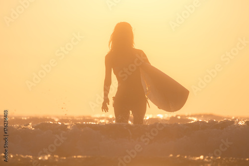 Woman with surfboard runs from the ocean during sunset