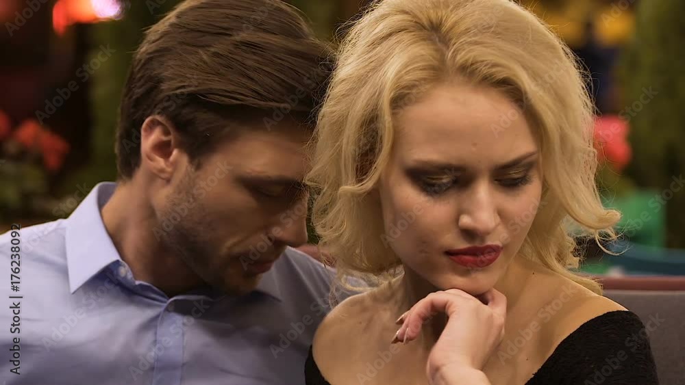 Angry blond female sitting next husband, man trying to touch apologetically Angry blond female sitting next husband, man trying to touch apologetically