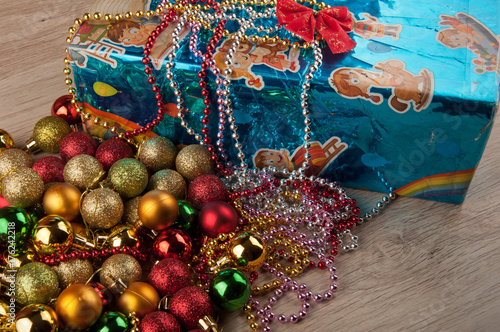 Christmas gifts. Blue glossy box with red bow-knot, decoration balls and beads laying on wooden table