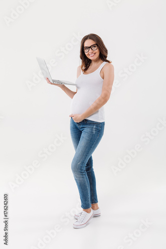 Happy pregnant woman wearing glasses using laptop