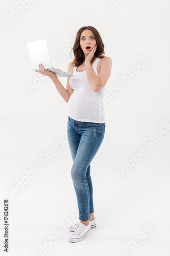 Shocked pregnant woman using laptop computer.