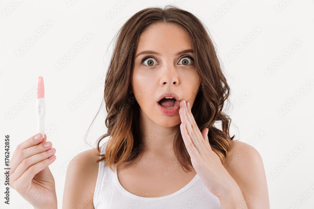 Shocked brunette woman holding positive pregnancy test Shocked brunette woman holding positive pregnancy test