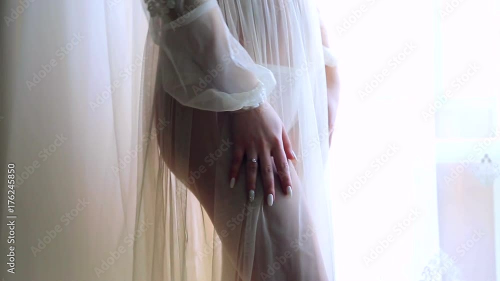 A young girl stands by the window in a night shirt. Legs close up of a beautiful model A young girl stands by the window in a night shirt. Legs close up of a beautiful model