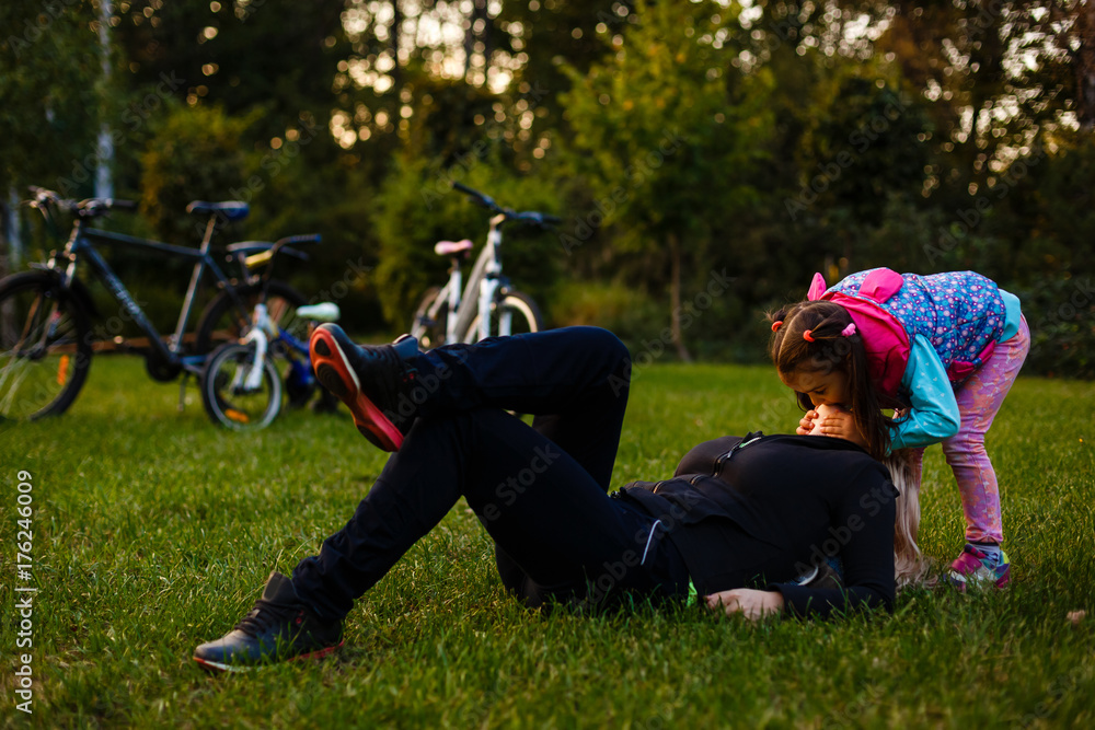 Happy mother and daughter lying outdoors smiling and hugging bicycles Happy mother and daughter lying outdoors smiling and hugging bicycles