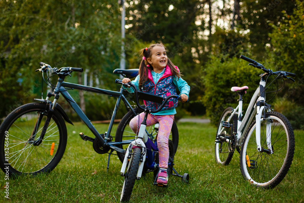 Little girl riding a bicycle in the park on the road covered with autumn oak and maple trees Little girl riding a bicycle in the park on the road covered with autumn oak and maple trees
