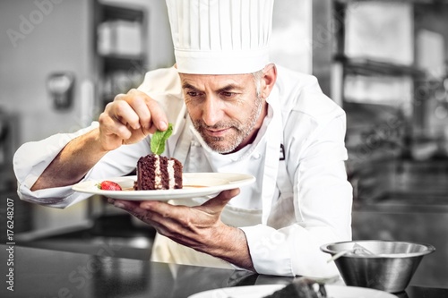 Bild auf Leinwand Concentrated male pastry chef decorating dessert in kitchen