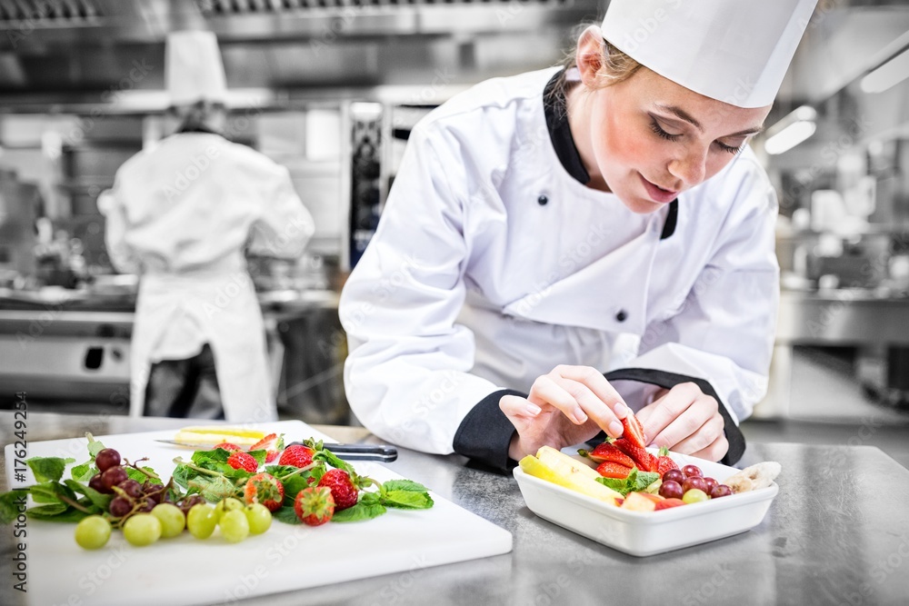 Female chef putting a strawberry in the fruit salad Female chef putting a strawberry in the fruit salad
