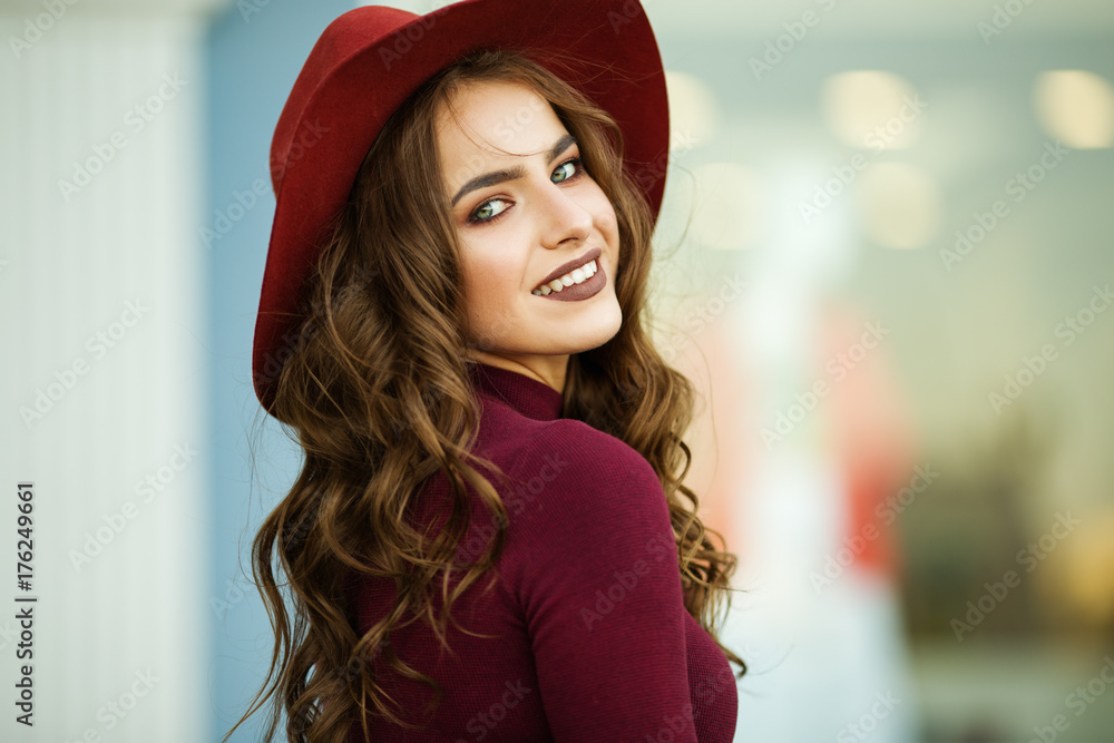 Naklejka premium Portrait of beautiful smiling elegant woman is wearing fashion autumn red clothes and hat infront of shop-window