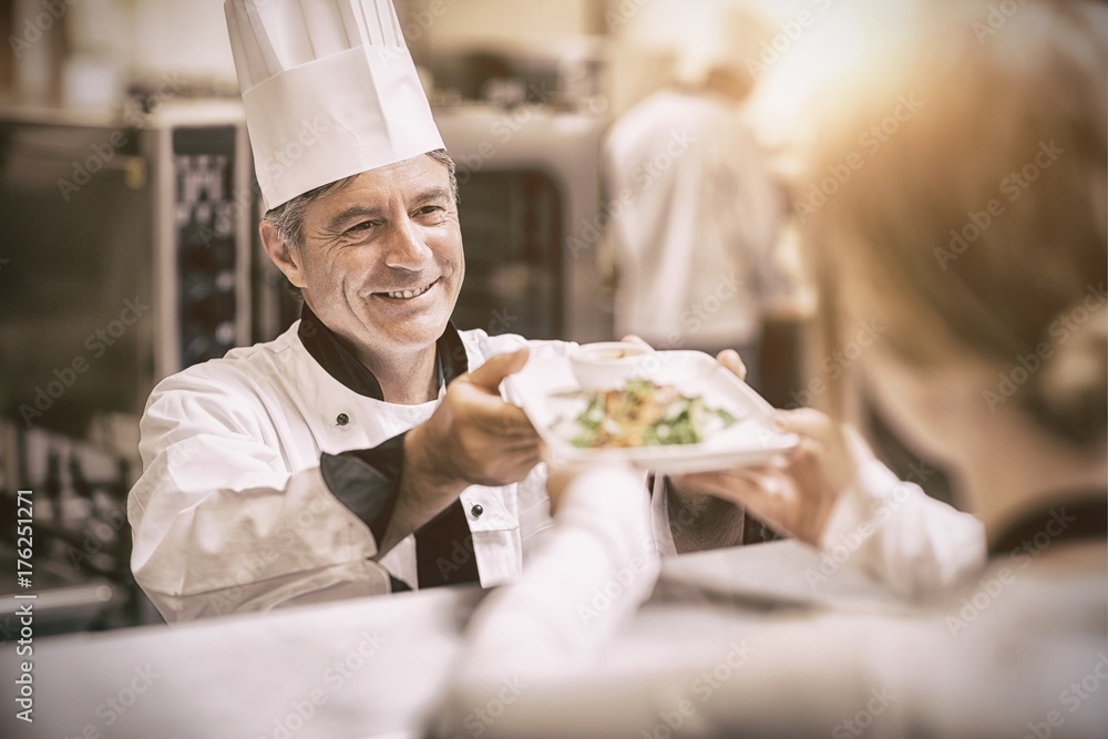 Chef handing dinner dish to waitress at order station Chef handing dinner dish to waitress at order station