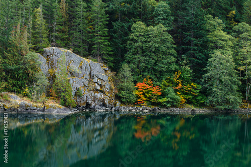 Autumn colors by a peaceful lake with a large rock formation and forest background.