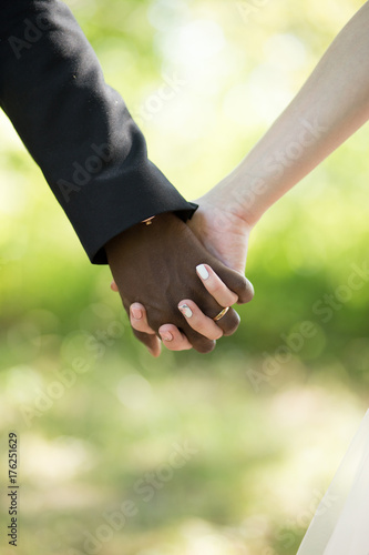 The hands of the newlyweds. The black-skinned groom and white-skinned bride Causian and African-American couple holding hand 