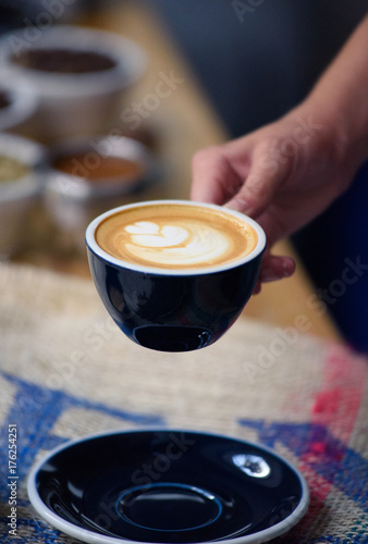 Perfectly brewed cappuccino and fresh roasted Arabica beans in the cozy atmosphere of a coffee shop. Professional barista or a client is going to taste a cup of coffee.