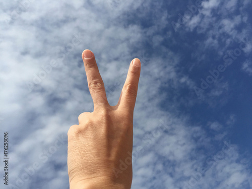 hand making victory sign against blue sky