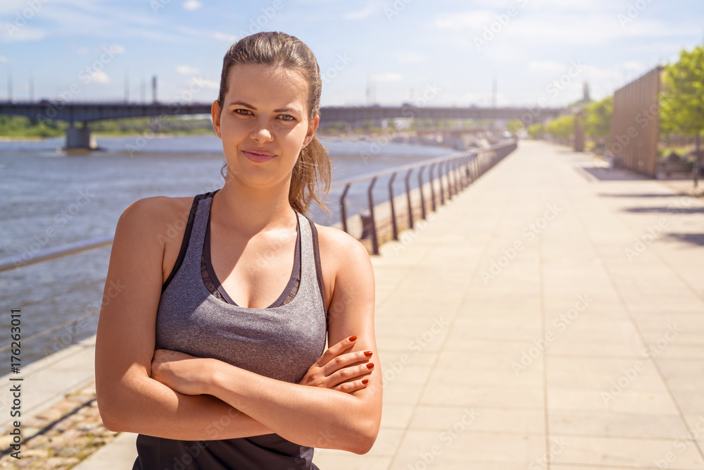 Young fit woman in sportswear standing with crossed arms in the city by the river smiling.