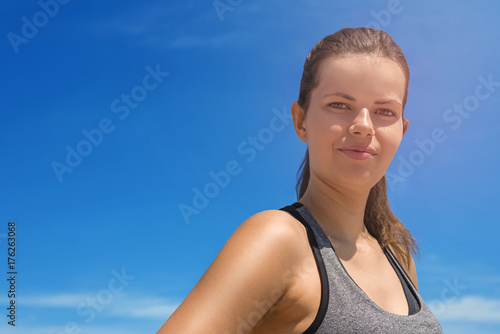 Young woman portriat in sportswear over blue sky in summer smiling. © Wisiel