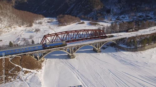 Passenger train going over bridge Polovina. Baikal lake Russia Siberia. Frozen ice  Transbaikalia TRANS-Siberian railway tourist attraction.  Beautiful High mountains. Sunny winter snow. Aerial Drone photo