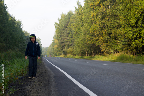 A boy walks along the roadside in the forest