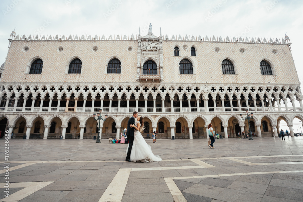 Bride and groom kiss on the empty square in Venice