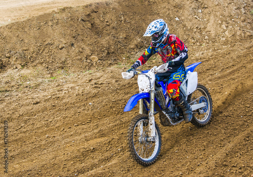The racer on a motorcycle participates in race motocrosses, goes on sand. Red blue suit. Close-up.