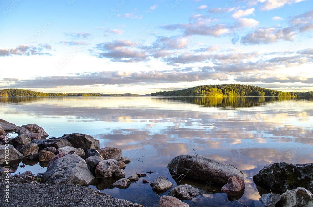 Beautiful sunset with reflection in water. Mirror summer lake. Lake Ladoga Karelia. Russia