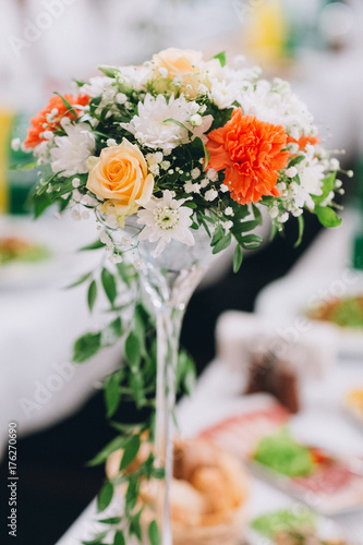 Fototapeta Naklejka Na Ścianę i Meble -  Tall glass vase with tender autumn flowers stands on long white dinner table