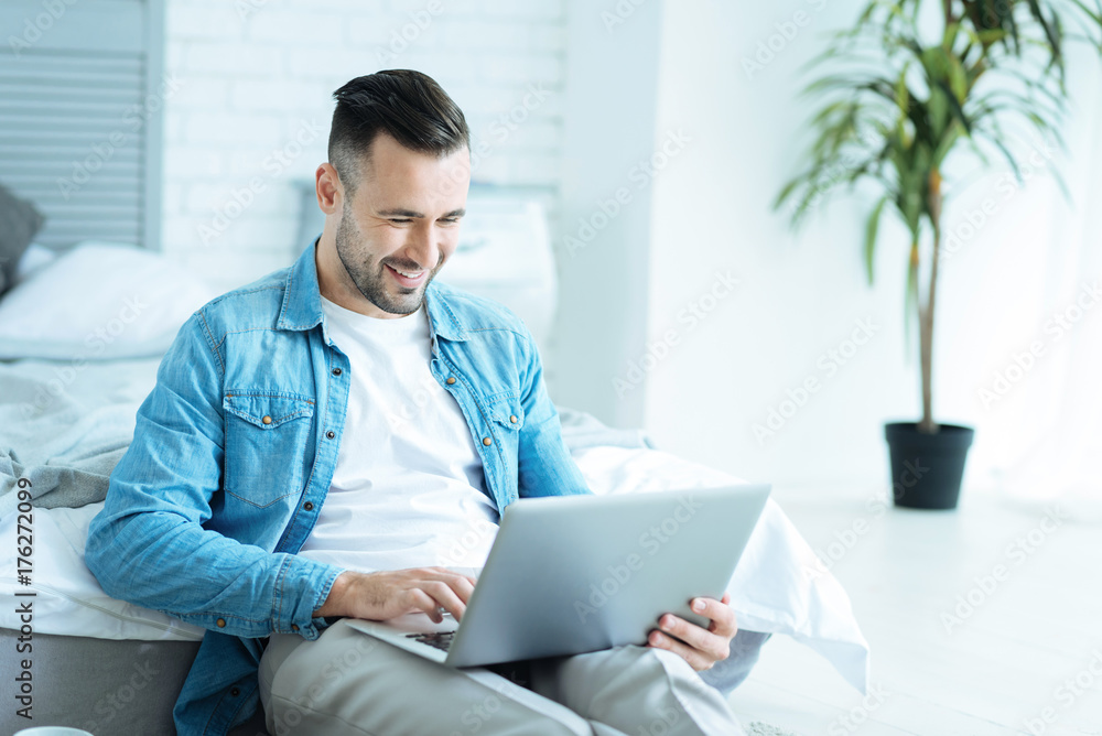Joyful man grinning broadly while using laptop Joyful man grinning broadly while using laptop
