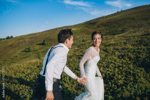 Cheerful newlyweds run on a green hill