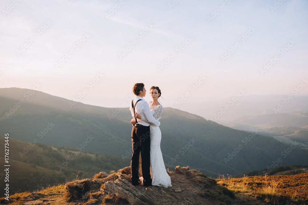 Bride and groom hug each other tender standing on the golden hill