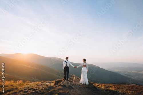 Bride and groom watch the sunset standing on the hill
