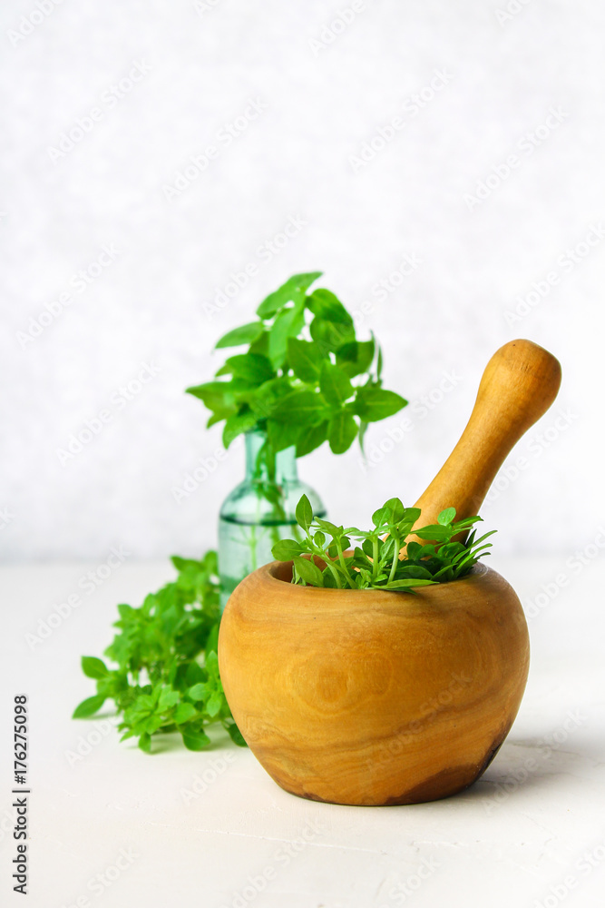 Green lemon basil in a wooden mortar on a light background. Behind the basil in the bottle.