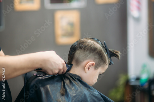 Little Boy Getting Haircut By Barber While Sitting In Chair At Barbershop.