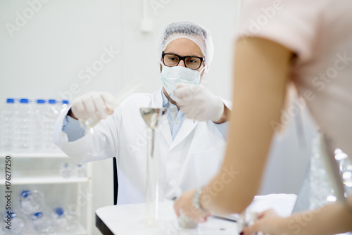 Scientist with face mask and glasses working with his assistant in the laboratory.