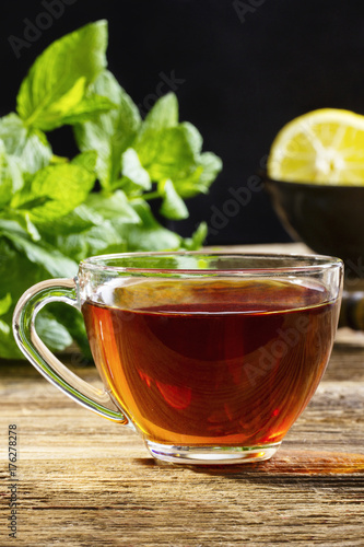 A cup of black tea on a wooden table with mint and lemon in the background