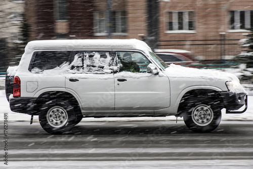 White big off road car riding in speed motion on the street in winter under the snow