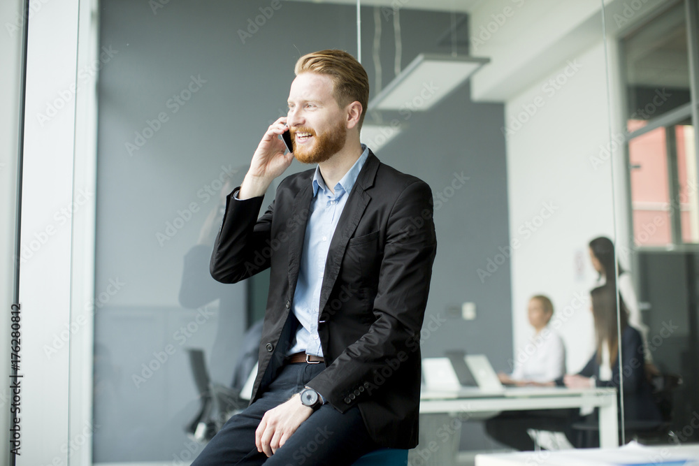 Businessman with ginger hair using mobile phone while other business people working in office