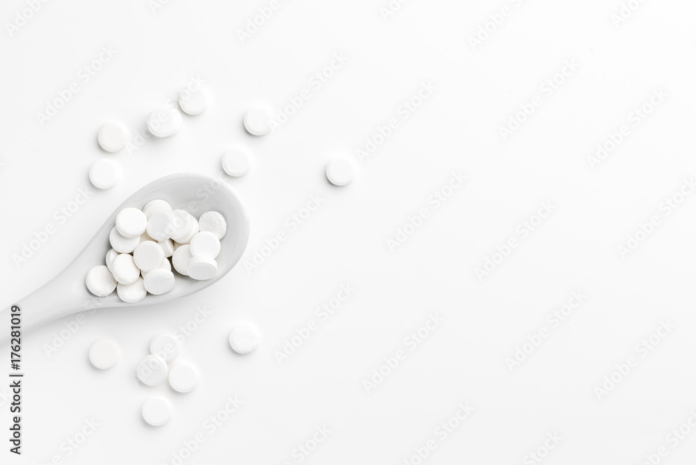 Pills on the spoon and scattered on the white surface