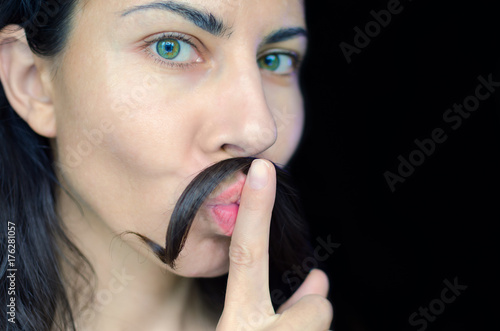 Portrait of a young woman with dark hair has put a strand of her hair on her upper lip. The concept of removing excess hair from women.