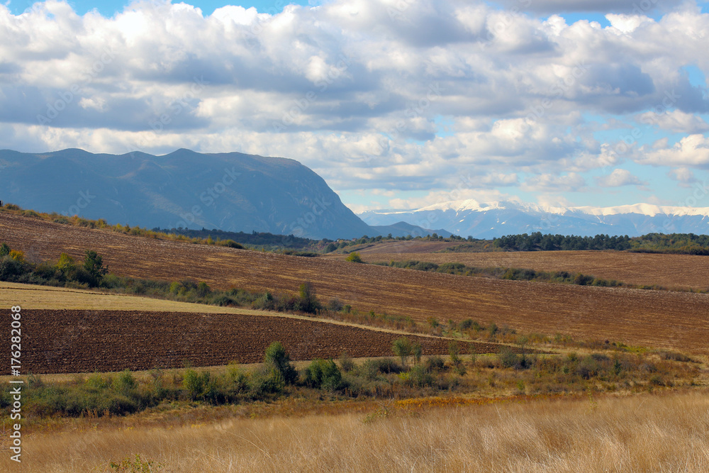 Autumn landscape. Fields, mountains and white clouds in the blue sky.