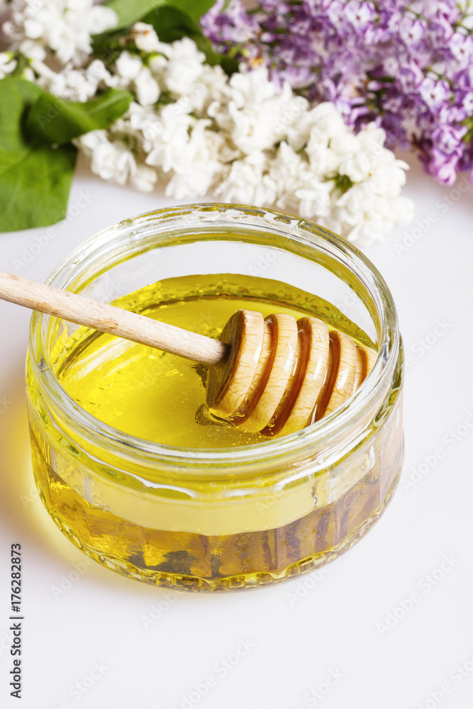 Organic honey in a glass jar and lilacs on a white Organic honey in a glass jar and lilacs on a white