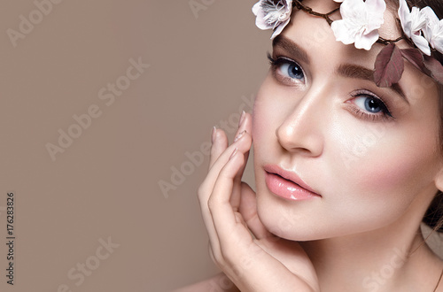 Beautiful woman portrait in tender colors. Young lady posing in studio with flowers on head. Pure skin, nice make up.