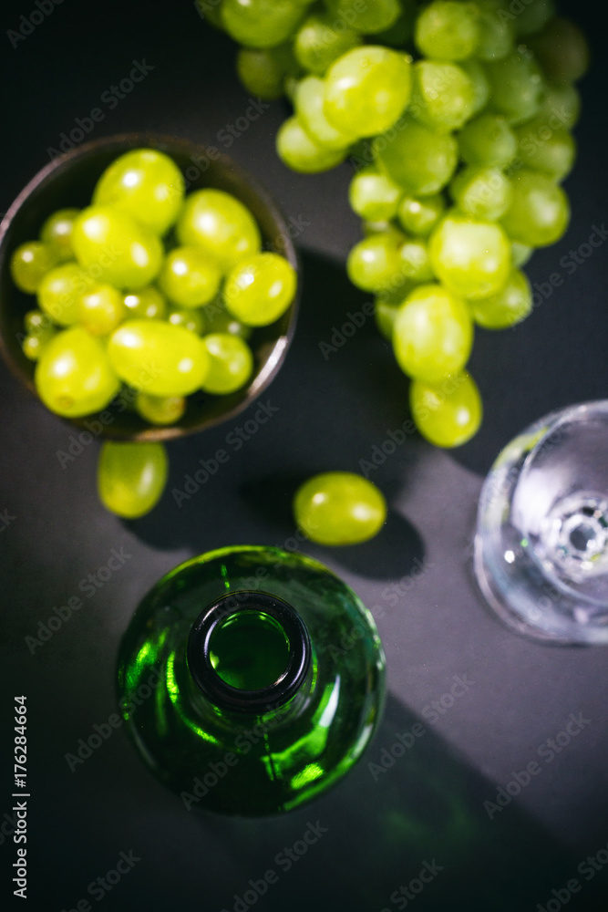 Bunch of white grapes, wine glass and a bottle on black table, view from top