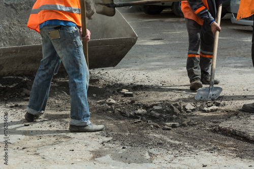Workers cleaned the old asphalt with shovels and toss the asphalt into the tractor's scoop